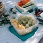 Picnic setup with containers of fruits, vegetables, and snacks arranged on a blanket, ideal for summer outings.